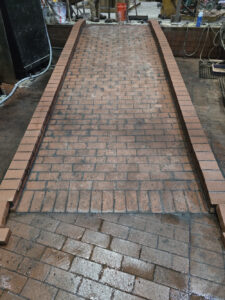Completed industrial brick ramp installation with full mortar joints and raised brick curbs on both sides.