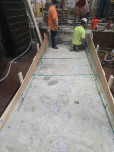 Workers preparing a formed concrete ramp with rebar reinforcement inside an industrial facility.