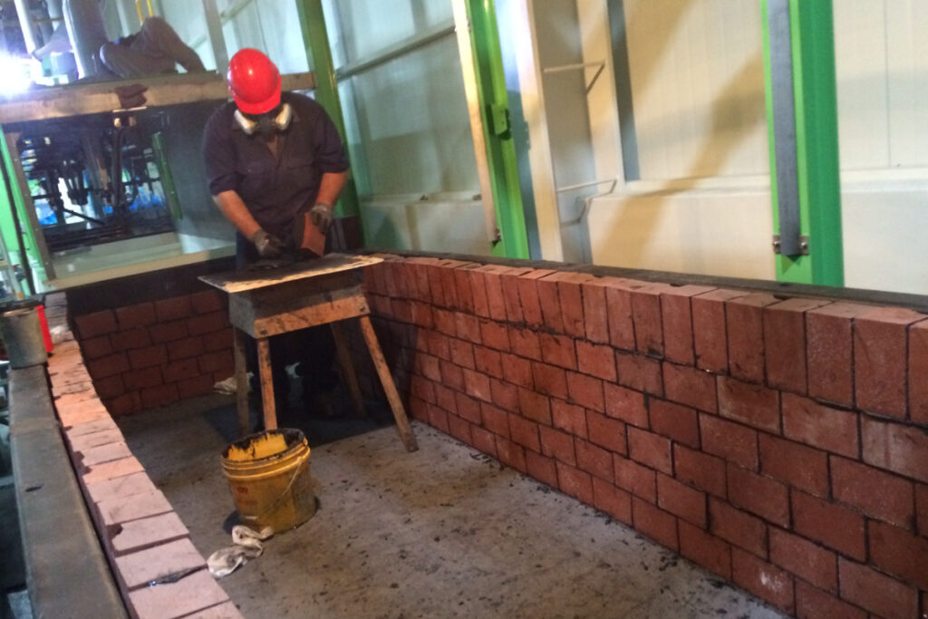 Worker installing acid brick lining inside an industrial containment basin using chemical-resistant mortar.